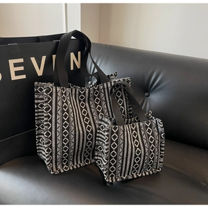 Close-up of black and white geometric woven tote bags in two sizes on a leather sofa