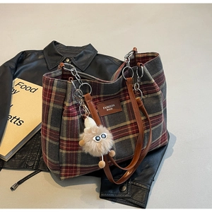 Detail of plaid tote bag with plush monster charm and leather straps on a jacket