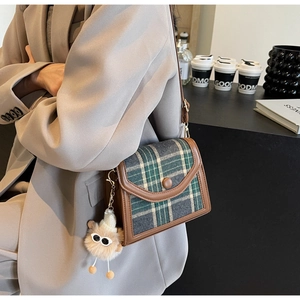 Detail of green plaid canvas shoulder bag with brown leather trim and plush charm detail