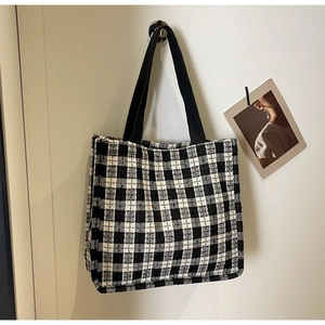 Detail of checkered canvas tote bag with black fabric handles on a minimalist wall