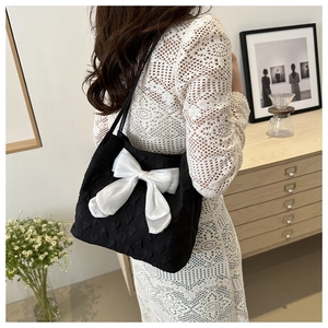 Detail of black jacquard tote bag featuring a large white satin bow on model's shoulder
