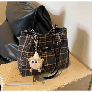 Detail of plaid tote bag featuring fuzzy charm and metallic chain handle connector