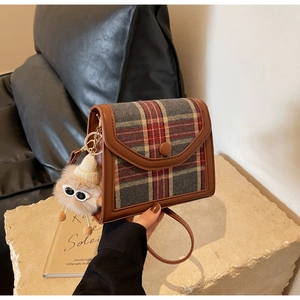 Close-up of retro plaid flap bag with brown leather trim and cute plush charm on stone