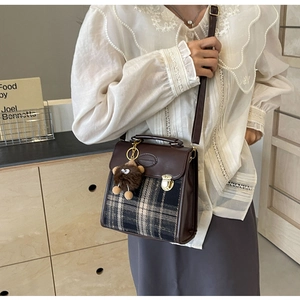 Detail of vintage plaid messenger bag with brown leather trim and cute bear charm