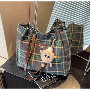 Detail of plaid tote bag with brown faux leather straps and cute plush monster charm