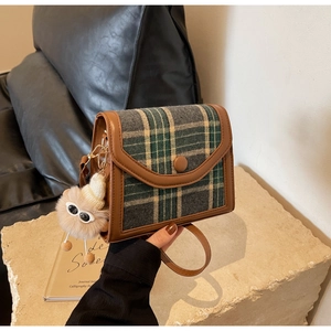 Detailed close-up of green tweed crossbody bag with leather trim and plush monster charm