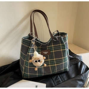 Detail of plaid tote bag with brown leather handles and a plush monster charm