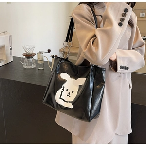 Detail view of a black glossy tote bag featuring a cute white cartoon rabbit print