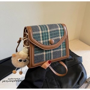 Detail of gray-green plaid texture with brown leather trim and plush ball charm