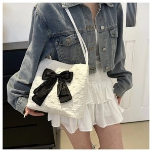 Detailed view of white star-embossed tote bag with large black satin bow on shoulder
