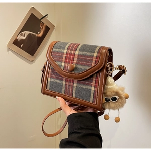 Detail of plaid crossbody bag with brown leather trim and cute furry monster keychain