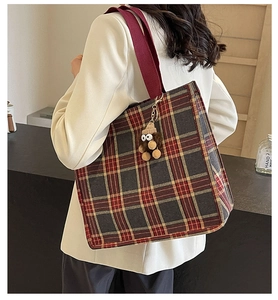 Detail of vintage plaid tote bag with red wide strap and plush monster charm