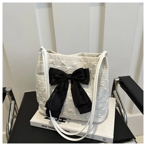 Detail of white bubble texture tote bag featuring a large decorative black bow on books