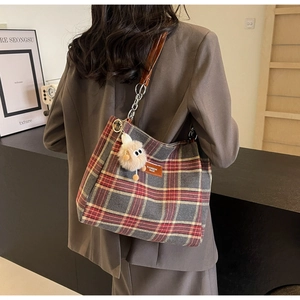Detail of plaid tote bag with leather strap, metal chain and plush monster charm