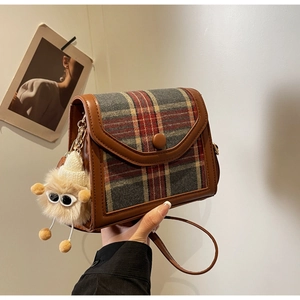 Detail of vintage plaid crossbody bag with brown leather trim and plush monster charm