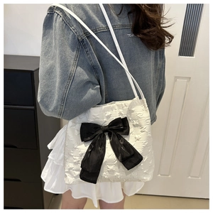 Close-up of white textured tote bag with a large black satin bow and slender shoulder straps