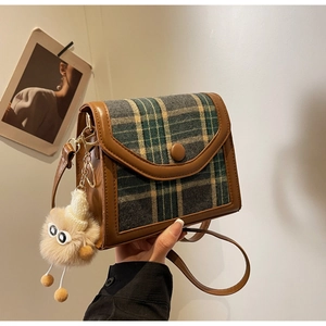 Detail of green plaid crossbody bag with a plush monster charm and leather trim edges