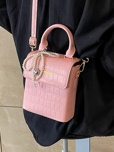 Pink crocodile pattern small square bag with pearl bow pendant and top handle shown on side