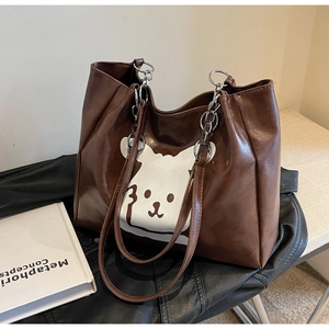 Detail of a brown tote bag featuring a white cartoon bear print and chain strap