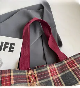 Detail of red and grey checkered canvas tote bag with woven handles and metal hooks