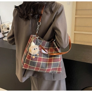 Detail of grey plaid tote bag featuring brown leather straps and plush bear charm