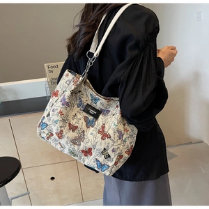Close-up of cream tote bag featuring colorful butterfly prints and metal chain strap
