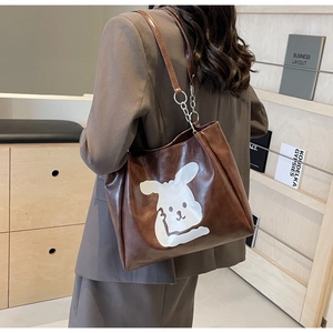 Detail of a brown PU leather tote bag featuring a cute white cartoon rabbit and chain strap