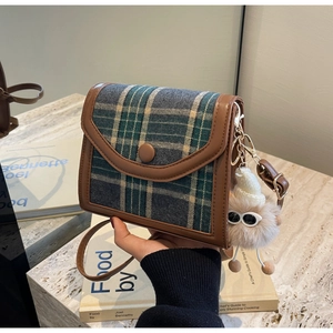 Detail of vintage plaid crossbody bag with brown leather trim and fuzzy charm on marble