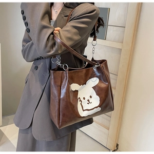 Brown tote bag with cartoon puppy print and silver chain strap shown on a gray suit