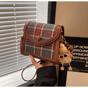 Close-up of vintage tartan crossbody bag with brown leather trim and plush monster charm