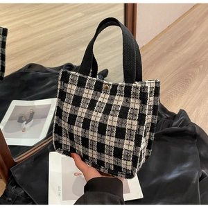 Detail of black and white checkered tweed tote bag with metal snap button and handle