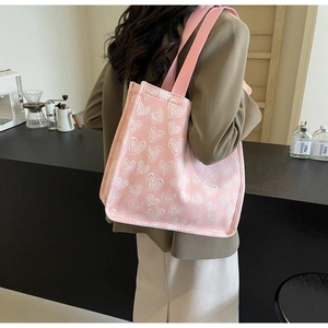 Detail of pink canvas tote bag with heart jacquard pattern shown on shoulder