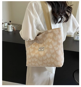 Detail of beige canvas tote bag with white heart embroidery worn by a model in a cafe