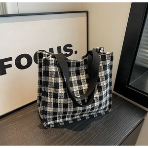 Detail of checkered tote bag with woven texture and black handles on a grey surface