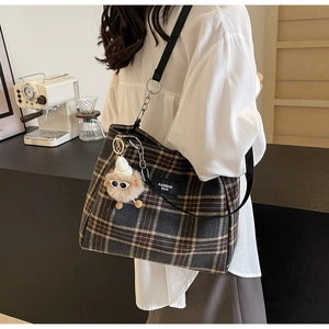 Detail of dark plaid tote bag with wide strap and cute sheep charm in a lifestyle setting