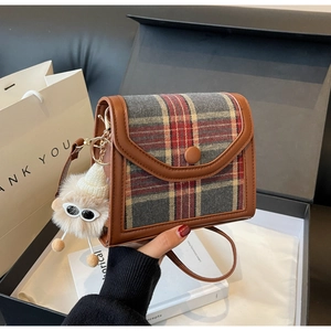 Detail of plaid crossbody bag with brown leather trim and cute plush monster charm