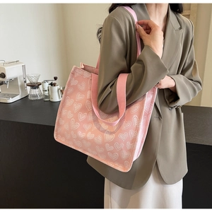 Borsa tote in tela rosa con cuori bianchi indossata da una modella in un caffè