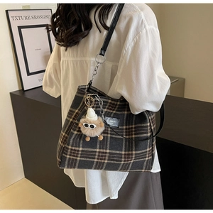Detail of grey plaid tote bag with plush charm and black leather strap worn by a model