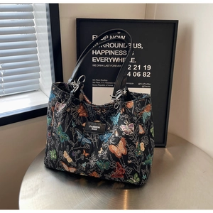 Close-up of black tote bag featuring colorful butterfly embroidery and leather tag
