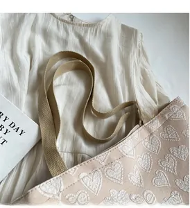 Close-up of beige tote bag showing white heart embroidery and brown woven handles