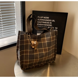 Detail of plaid canvas tote bag with check pattern and plush monkey charm on silver table