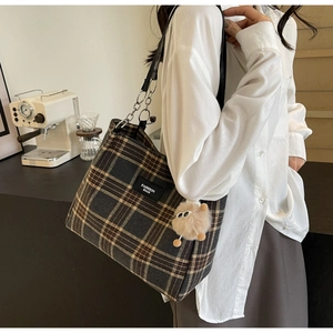 Detail of plaid tote bag featuring leather chain straps and a plush bear pendant