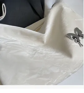 Détail du sac en cuir verni plissé crème avec un pendentif papillon en métal argenté