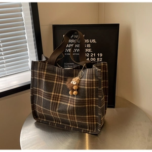 Detail of grey plaid canvas tote bag featuring brown plush doll charm and sturdy handles