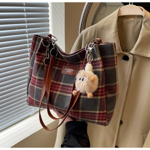 Detail of checkered tote bag with leather handles and plush charm in warm light