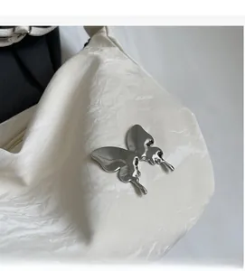 Gros plan sur la texture plissée blanche avec un papillon métallique argenté sur le sac à bandoulière