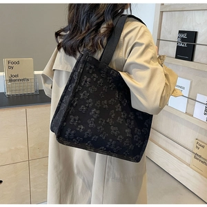 Close-up of black tote bag with embossed floral texture on a model wearing a trench coat