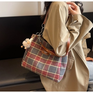 Detail of red and grey plaid tote bag with brown leather strap and plush doll charm