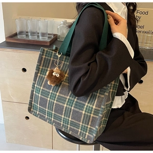 Close-up of green plaid canvas tote bag with a brown plush monster charm on shoulder