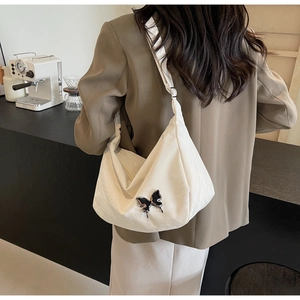 Détail d'un sac bandoulière demi-lune crème avec ornement papillon porté par un modèle